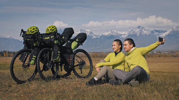 The man and woman travel on mixed terrain cycle touring with bikepacking The two people journey with bicycle bags Sport bikepacking bike sportswear in green black colors Mountain snow capped