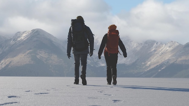 The man and woman with backpacks walking on a snowy mountains background