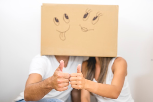 Photo the man and woman with a carton box on the heads thumb up