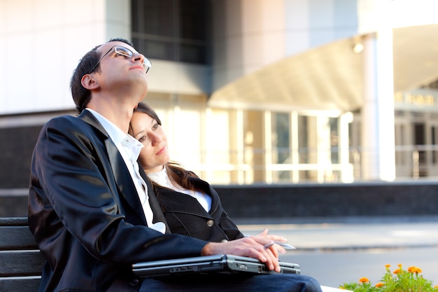 Man and woman with laptop and sitting on bench