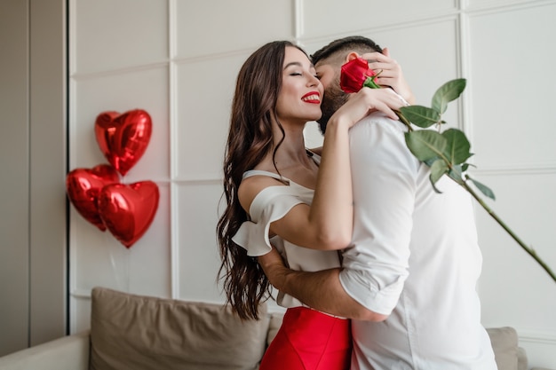 Man and woman with red rose at home with heart shaped balloons in apartment