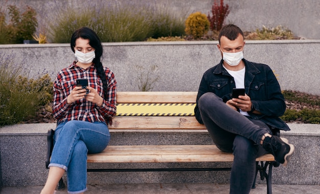 Photo man and woman with smartphones sitting on bench during pandemic