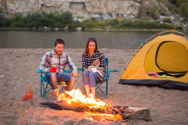 Man and woman with their cat sit near a fire