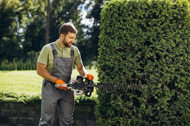 Man worker cutting bushes with an electric saw in the yard