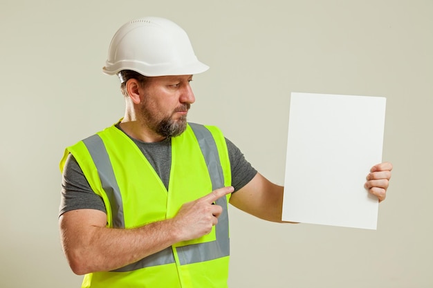 Man worker in a vest and a white construction helmet hat with a white sheet in his hands on a white