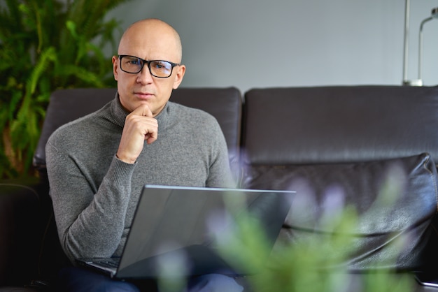 Man working on a blank laptop on a comfortable sofa at home.