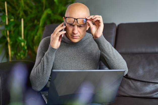 Man working on a blank laptop on a comfortable sofa at home.