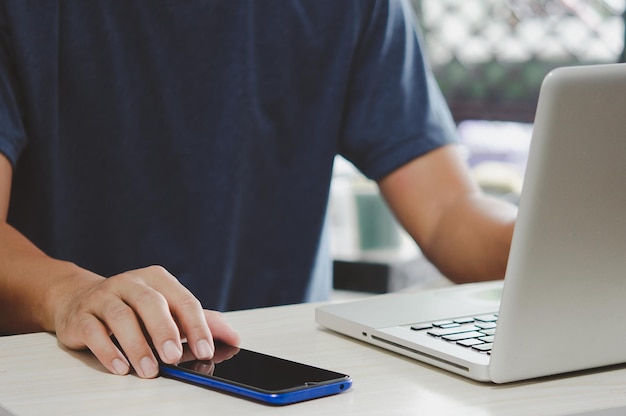 Man working at computer desk pressing mobile phone