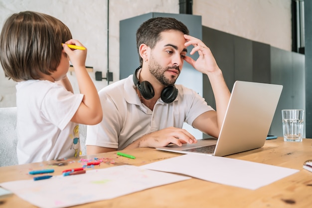 Man working from home while taking care of his son. Stay at home. Working from home during covid-19 quarantine.