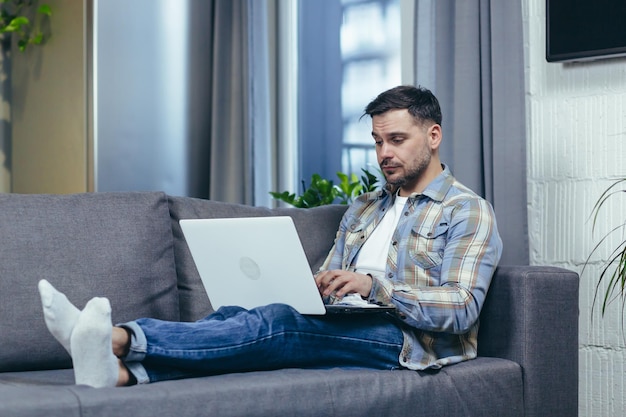 Man working at home sitting on sofa and talking on video call looking at laptop screen