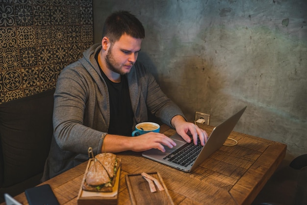 Man working on laptop in cafe breakfast sandwich and coffee