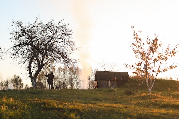 Man works in the garden and picks up autumn leaves in the picturesque rural landscape