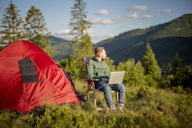 Man works on laptop at campsite in the mountains