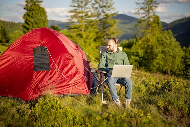 Man works on laptop at campsite in the mountains