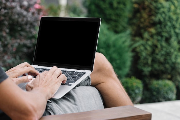 A man works in nature sitting in a chair with a laptop