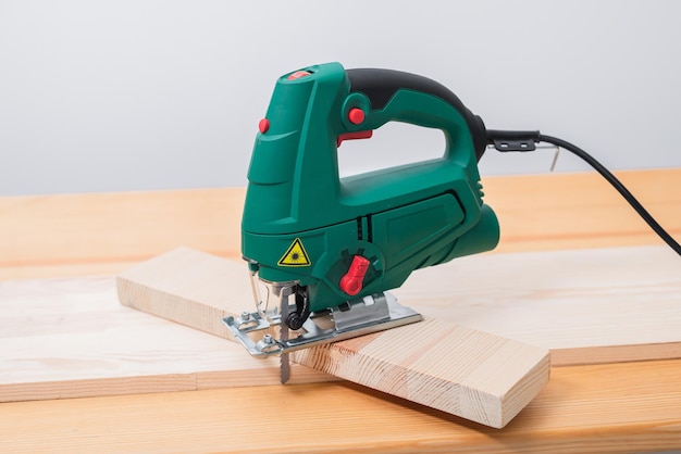 A man works with an electric jigsaw for wood on a wooden table with and without gloves and measures with a tape measure