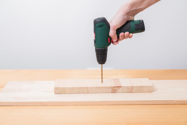 A man works with an electric screwdriver on a wooden table also makes measurements with a tape measure