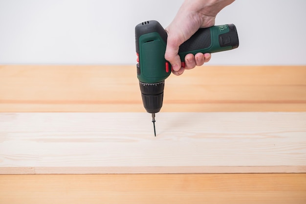 A man works with an electric screwdriver on a wooden table