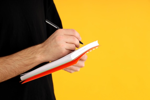 Man writes in a notebook on a yellow background