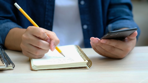 Man writing on notebook while using mobile phone