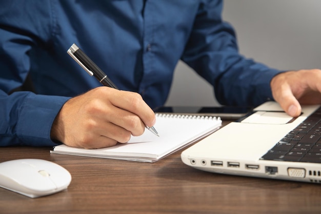 Man writing on notepad and using laptop computer