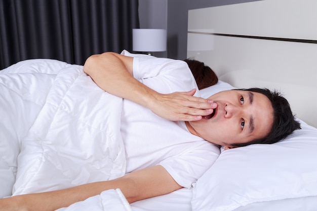 man yawning and his wife sleeping on bed