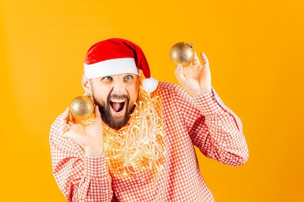 A man on a yellow background holds toys for the Christmas tree, golden balls, she opened her mouth and smiles slyly