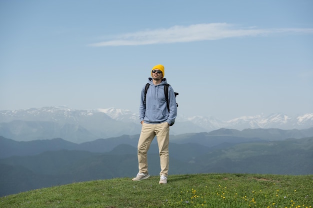 Man in yellow hat and blue hoodie concuered the summit against the snowy mountain peaks