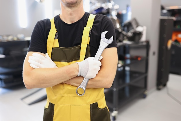 A man in a yellow overalls holds a wrench closeup professional mechanic in garage repairing