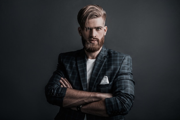 Man of your dreams! Handsome man keeping arms crossed and looking at camera while standing against grey background