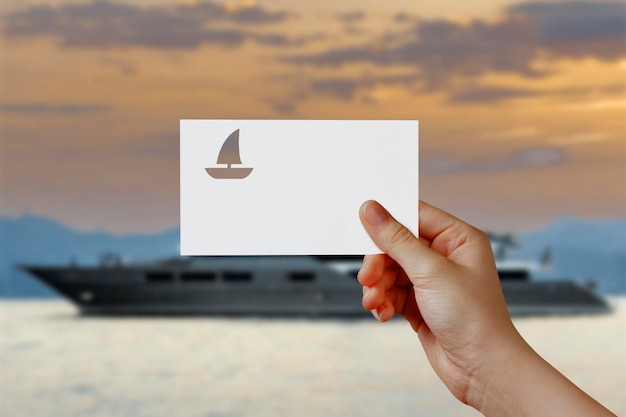 Man39s hand holding yatch symbol paper in front of sea Concept of journey travel dream freedom Hand is holding paper boat against yatch station with empty space for text