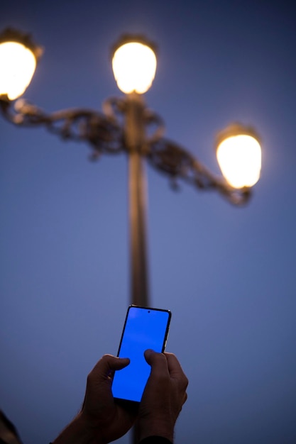 Man39s hands using cell phone screen outdoors with antique street lamps