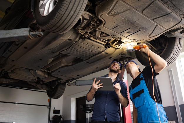 Manager checks data on a tablet computer and explains the breakdown to mechanic car service employee