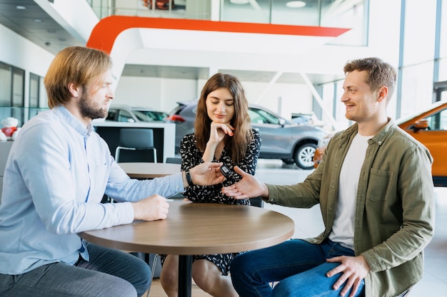 The manager of the dealership gives the keys to the new car to her husband and the wife is sitting next to him Buying a family car