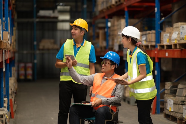 Manager handicapped in wheelchair man employee using tablet check stock work at warehouse Worker wearing high visibility clothing and hard hat helmet and checking count up goods boxes for delivery