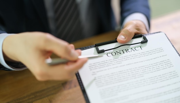 Manager holding out document contract on clipboard and pen for signing closeup