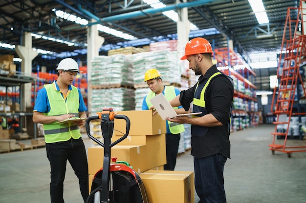 Manager man using laptop check stock cardboard on forklift and coworker at warehouse Worker wearing high visibility clothing and hard hat helmet to checking count up goods or boxes for delivery