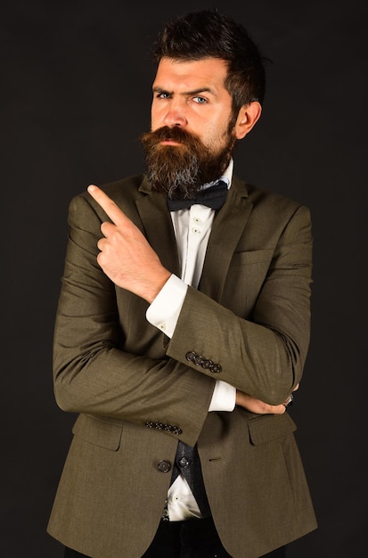 Manager or speaker with stylish beard and moustache. Businessman with serious face points up. Man in retro smart suit and bow tie on brown background. Business and vintage style concept.