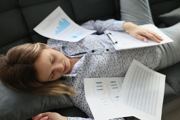 Manager woman covered with papers from financial report sleeping on sofa concept of overwork