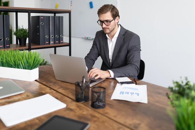 Manager works at a computer in glasses with papers on a table in a strong office