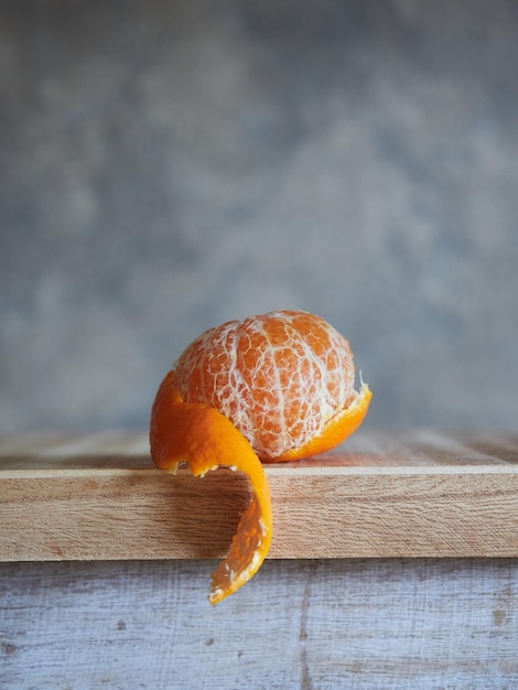 Mandarin with partially peeled skin on wood and gray textured background