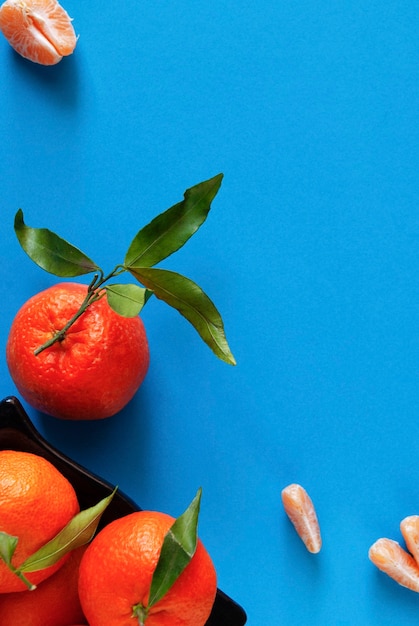 Mandarins on a blue surface next to tangerine slices.