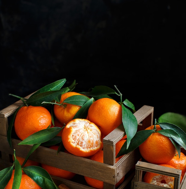 Mandarins with leaves in a box on a dark background