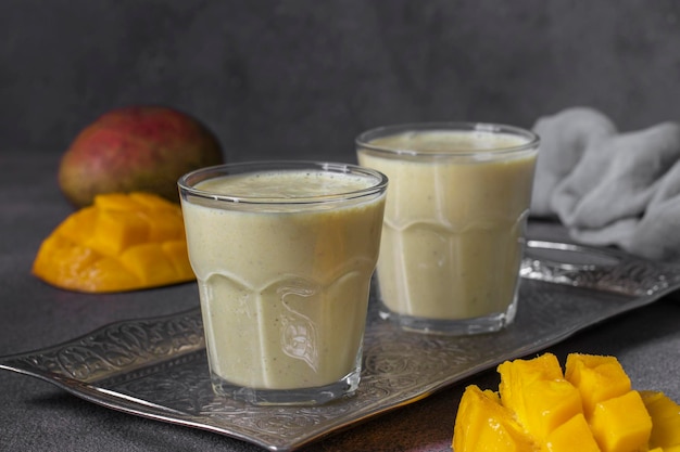 Mango lassi in two glasses on gray background Freshness indian lassi made of yogurt spices mango and ice