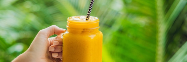 Mango smoothie in a glass Mason jar and mango on a green background. Mango shake. Tropical fruit concept BANNER, long format