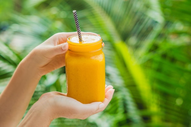 Mango smoothie in a glass Mason jar and mango on a green background. Mango shake. Tropical fruit concept