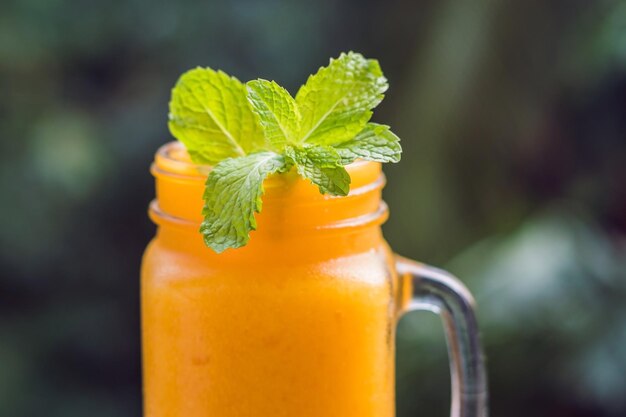 Mango smoothie in a glass Mason jar and mango on a green background. Mango shake. Tropical fruit concept