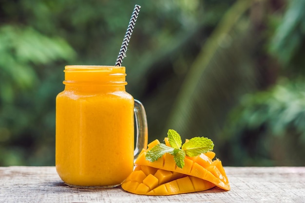 Mango smoothie in a glass Mason jar and mango on a green background. Mango shake. Tropical fruit concept