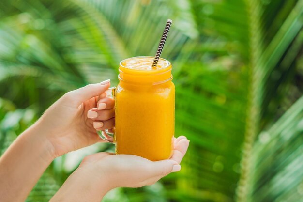 Mango smoothie in a glass Mason jar and mango on a green background. Mango shake. Tropical fruit concept