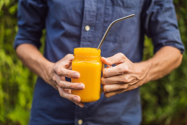 Mango smoothie and steel drinking straw in hands